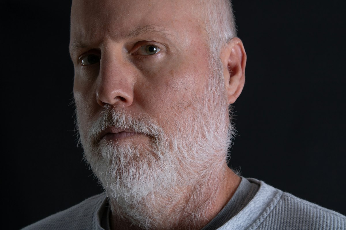 Retrato de um homem com barba grisalha curta sobre fundo escuro