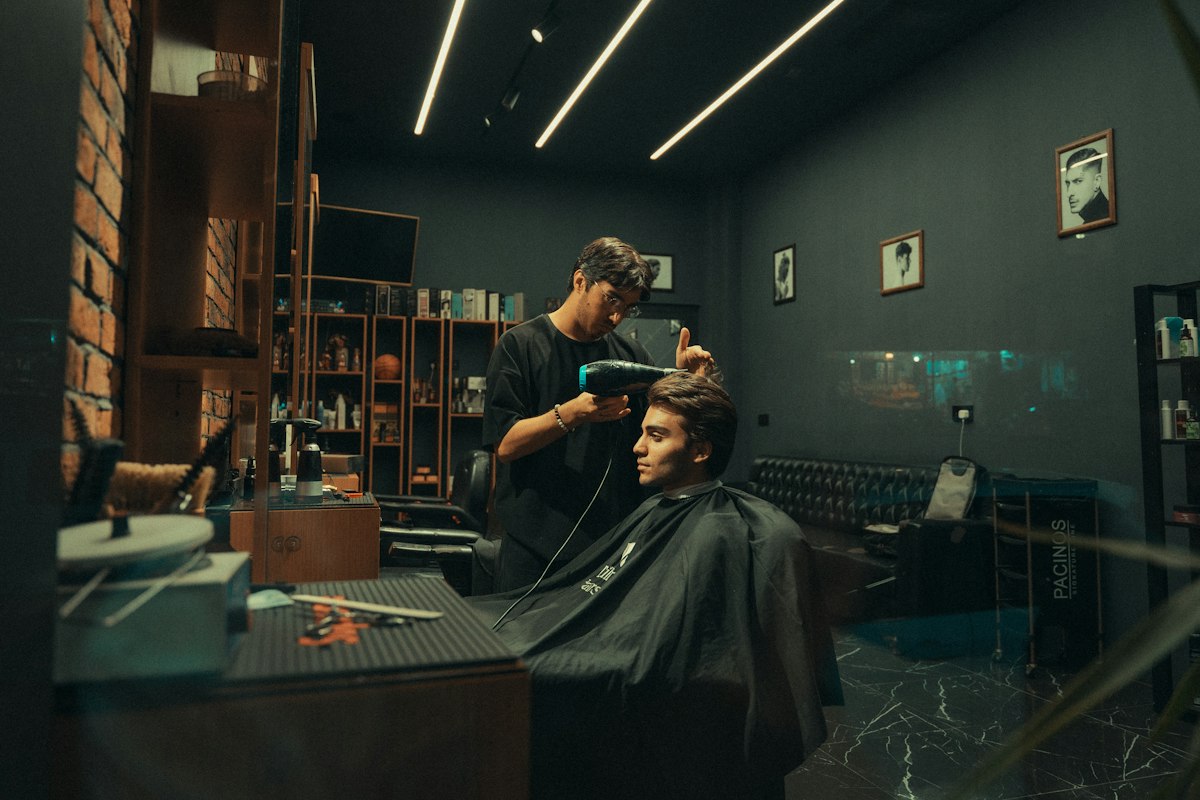 Barbeiro a pentear e secar o cabelo de um cliente numa barbearia com luz baixa