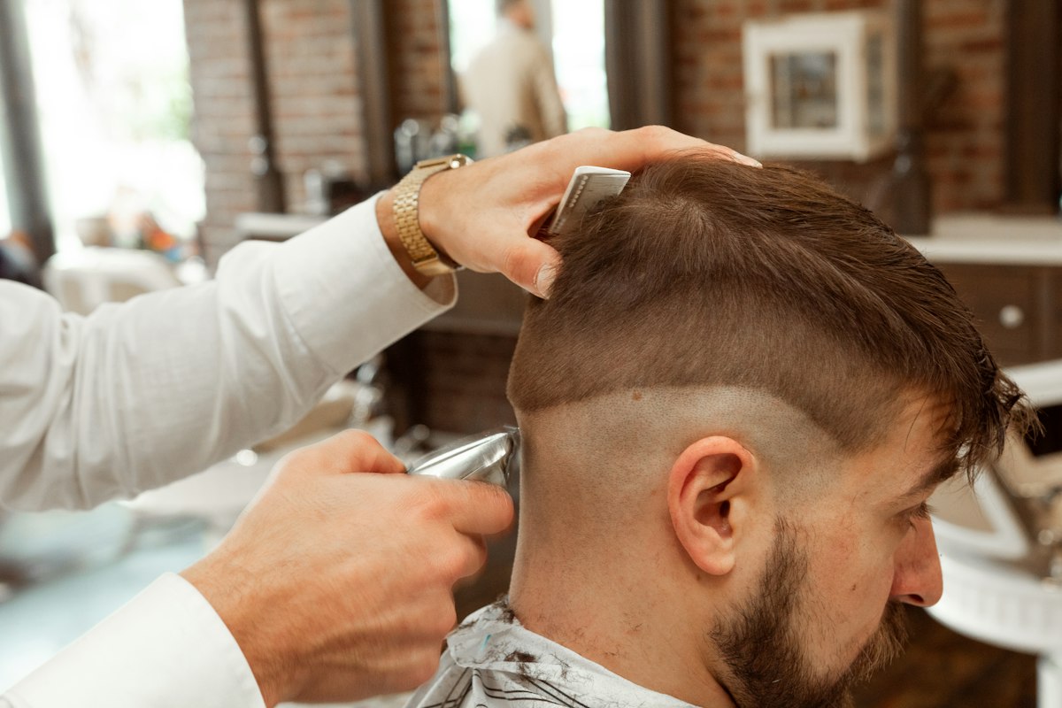 Barbeiro a cortar as laterais com máquina a um cliente de barba