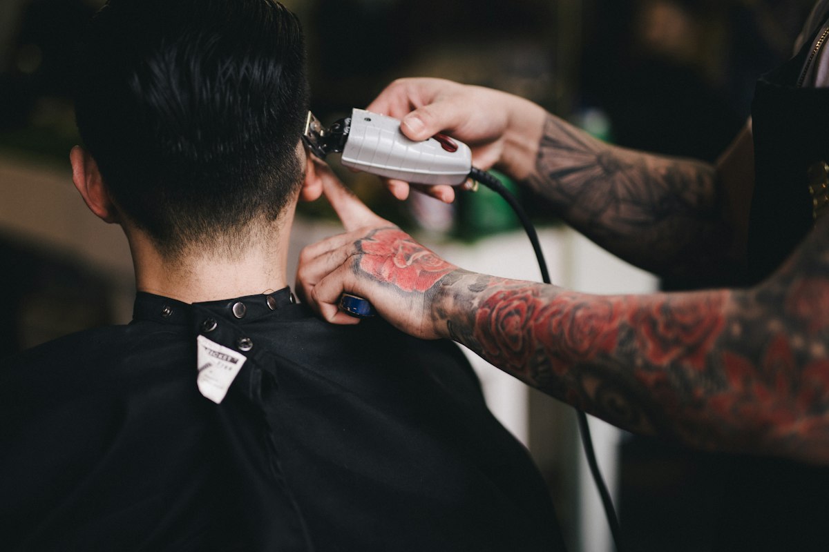 Barbeiro tatuado a passar a máquina na nuca de um cliente