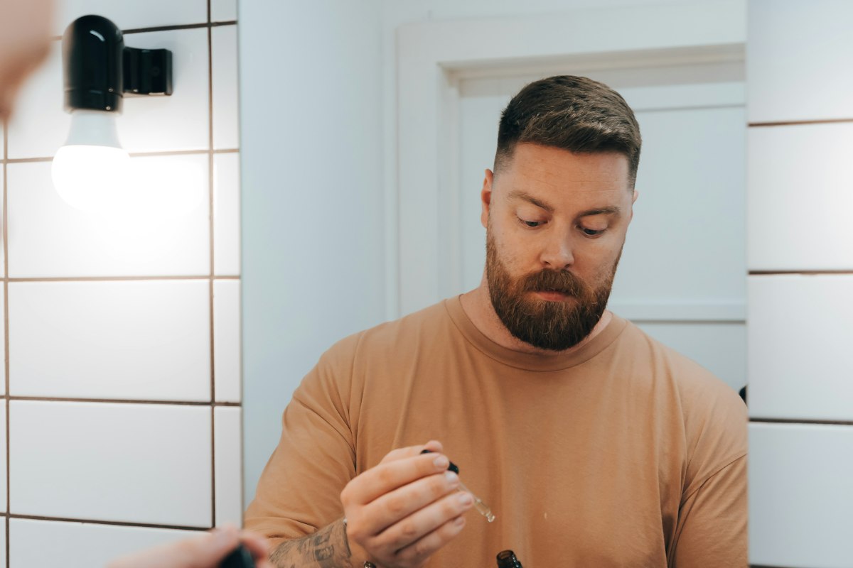 Homem de barba ao espelho da casa de banho a aplicar um produto no rosto