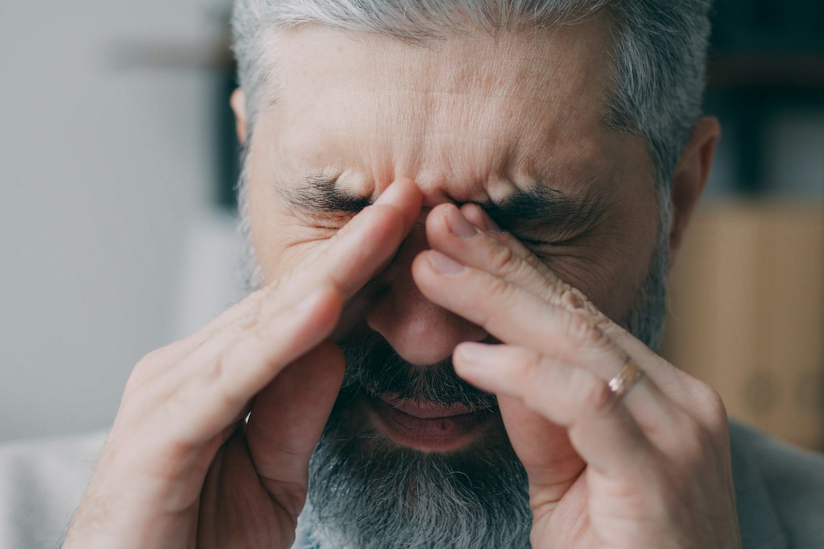 Homem grisalho de barba a esfregar os olhos cansados com as mãos