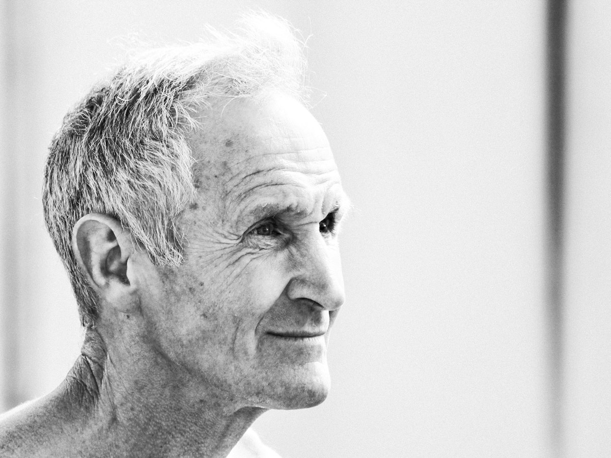 Retrato a preto e branco de um homem de cabelo grisalho, de perfil, a sorrir