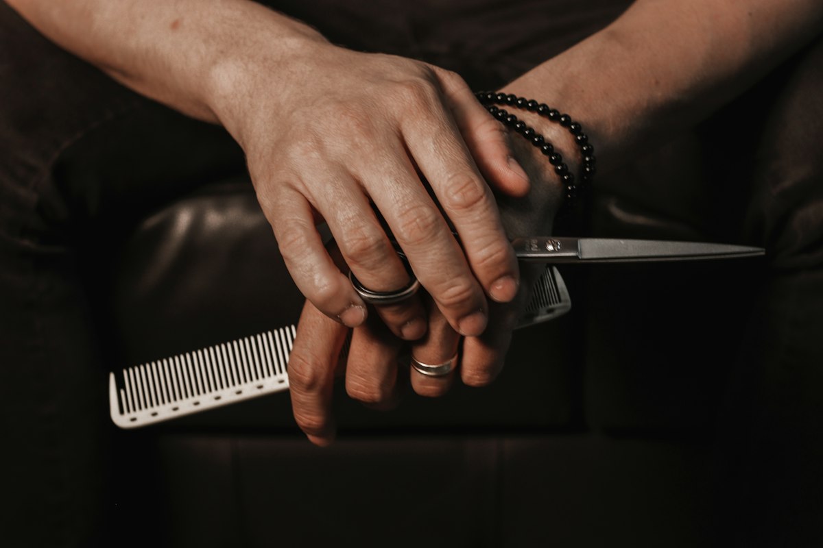 Mãos de barbeiro a segurar pente e tesoura
